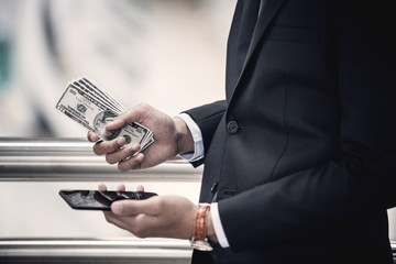 Businessman holding US Dollar bills while using smartphone for online banking. e-commerce and investment concept.