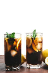 Cuba Libre cocktail with rum, cola, mint, lemon and ice in the glass on a brown table and white background