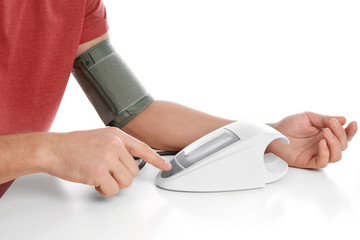 Fototapeta premium Man checking blood pressure with sphygmomanometer at table against white background, closeup. Cardiology concept