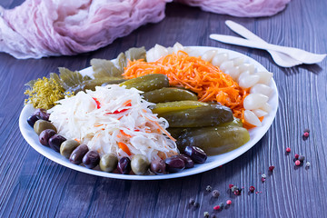 Assorted pickled and fermented vegetables in a white plate on a brown wooden background.