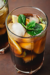 Cuba Libre cocktail with rum, cola, mint, lemon and ice in the glass on a brown background