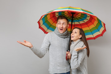 Couple girl guy in gray sweaters scarves together under umbrella isolated on grey wall background,...