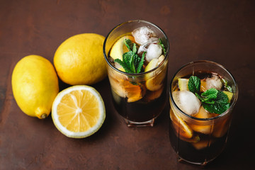 Cuba Libre cocktail with rum, cola, mint, lemon and ice in the glass on a brown background