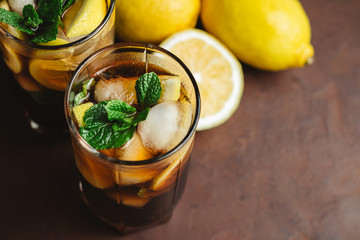 Cuba Libre cocktail with rum, cola, mint, lemon and ice in the glass on a brown background