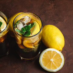 Cuba Libre cocktail with rum, cola, mint, lemon and ice in the glass on a brown background