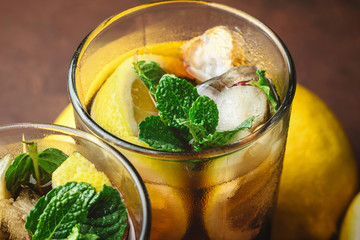 Cuba Libre cocktail with rum, cola, mint, lemon and ice in the glass on a brown background