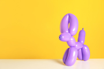 Animal figure made of modelling balloon on table against color background. Space for text