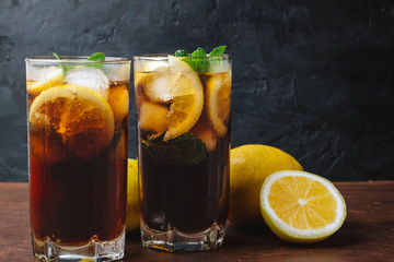 Cuba Libre cocktail with rum, cola, mint, lemon and ice in the glass on a brown table and black background