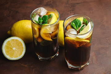 Cuba Libre cocktail with rum, cola, mint, lemon and ice in the glass on a brown background