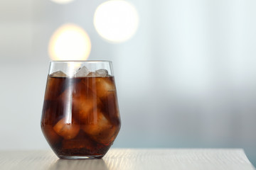 Glass of cola with ice on table against blurred background. Space for text