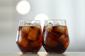 Glasses of cola with ice on table against blurred background