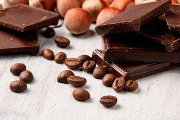 pieces of dark chocolate, hazelnuts and coffee beans on a white wooden table