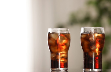 Glasses of cola with ice on table against blurred background. Space for text