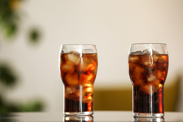 Glasses of cola with ice on table against blurred background