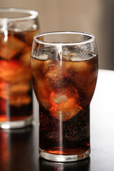 Glass of cola with ice on table against blurred background