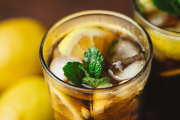 Cuba Libre cocktail with rum, cola, mint, lemon and ice in the glass on a brown background