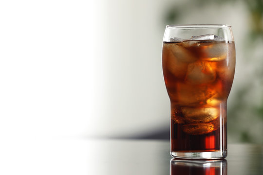 Glass of cola with ice on table against blurred background. Space for text