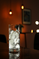 Glass with ice cubes on table in dark room