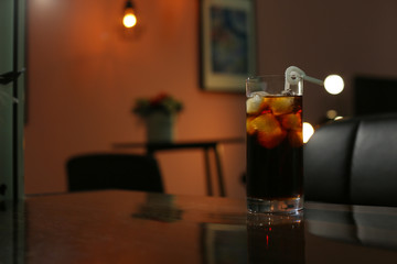 Glass of cold cola on table in dark room. Space for text