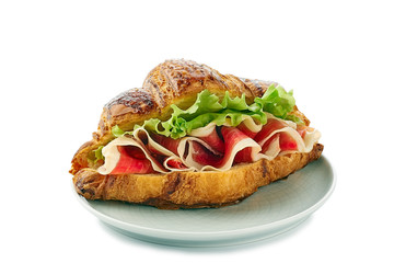 Plate with croissant sandwich with jamon of ham and lettuce on white