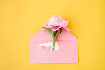 Peony flower in a pink envelope on a yellow background, top view. Romantic card by a holiday
