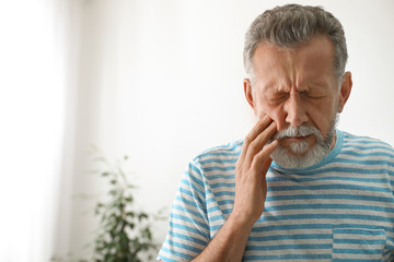 Mature man suffering from strong tooth pain at home, space for text