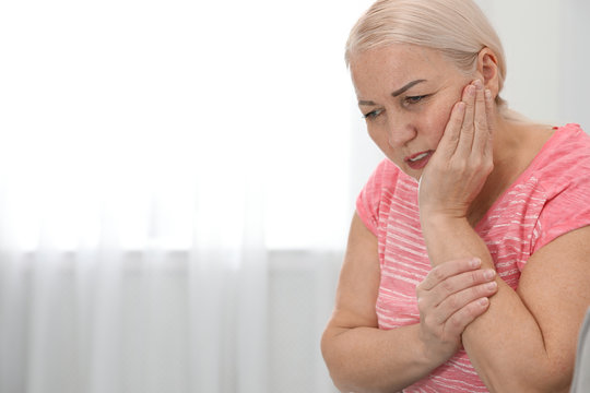 Mature woman suffering from strong tooth pain at home, space for text