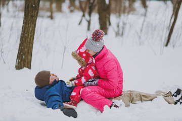 Happy family woman, man and little girl in warm clothes lying, sitting on snow in park or forest outdoors. Winter fun, leisure on holidays. Love childhood relationship family people lifestyle concept.