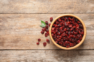Bowl with cranberries on wooden background, top view with space for text. Dried fruit as healthy snack