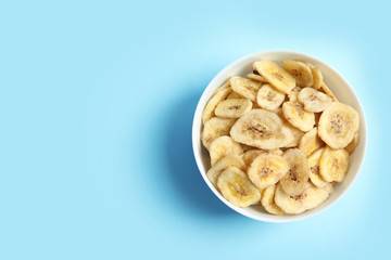 Bowl with banana slices on color background, top view with space for text. Dried fruit as healthy snack