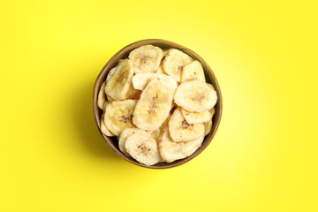 Wooden bowl with sweet banana slices on color background, top view. Dried fruit as healthy snack
