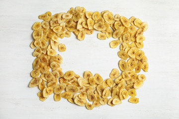 Frame made of sweet banana slices on wooden background, top view with space for text. Dried fruit as healthy snack