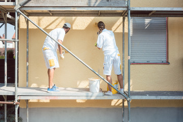 Back view of man and woman painter working coloring wall yellow