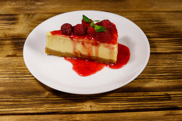 Piece of tasty New York cheesecake with raspberries and raspberry jam in a white plate on wooden table