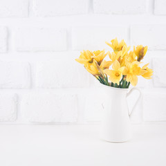 Jar with narcissuses at the white brick background. Spring, mothers day and Easter concept
