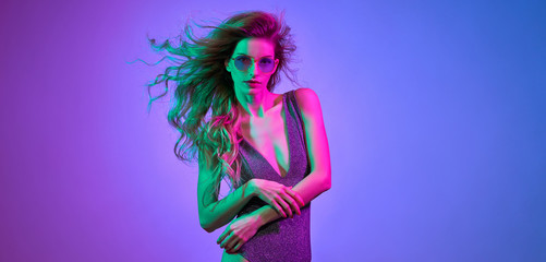 High fashion. Woman in colorful bright Neon purple light. Glamour sexy disco girl in Trendy bodysuit, Stylish sunglasses, makeup. Creative fashionable portrait