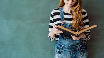 Female student reading book on green chalkboard