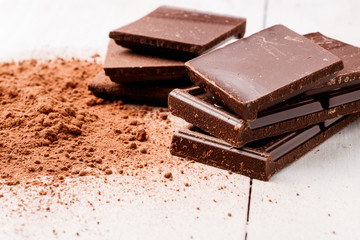 pieces of dark chocolate and cocoa powder on a white wooden table
