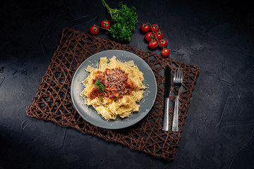Italian pasta with tomato sauce, cheese parmesan and basil on plate on dark table. Top view