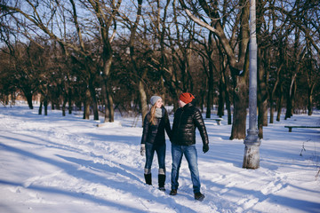 Fototapeta na wymiar Happy smiling couple woman and man in winter warm clothes looking at each other, walking in snowy park or forest outdoors. Winter fun, leisure on holidays. Love relationship people lifestyle concept.