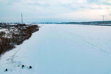 Northern winter landscape in cold blue tones: a frozen river against a low sky, fishermen are engaged in winter fishing