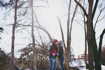 Young couple in love woman and man in warm clothes kissing, holding hands, walking in snowy city park or forest outdoors. Winter fun, leisure on holidays. Love relationship people lifestyle concept.