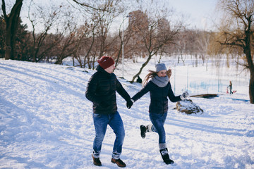 Fototapeta na wymiar Funny young couple woman and man in warm clothes running, holding hands, walking in snowy city park or forest outdoors. Winter fun, leisure on holidays. Love relationship people lifestyle concept.