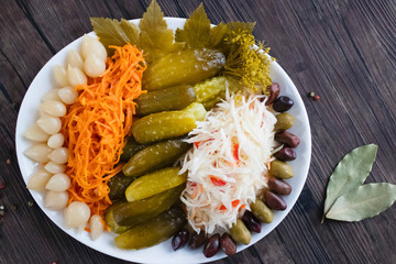 Assorted pickled and fermented vegetables in a white plate on a brown wooden background.