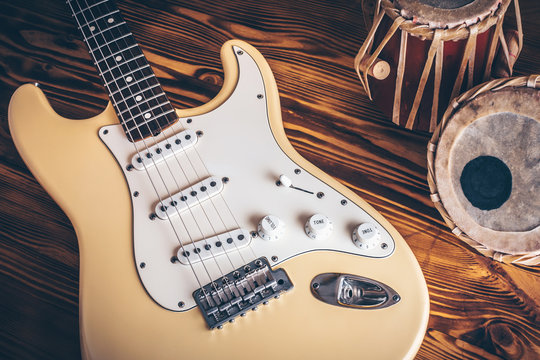 Vintage electric guitar and indian percussion instrument (tabla) on wooden background.