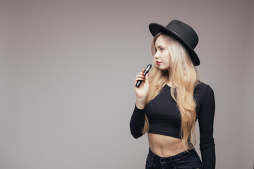 Portrait of sexy young hipster smoking vaping girl isolated on gray background. Vapor concept....