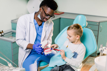 The child boy in dentist's chair having fun while brushing teeth with a male African American doctor