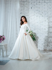 Young attractive bride woman in gorgeous white wedding dress posing in the bright studio with wedding decoration.