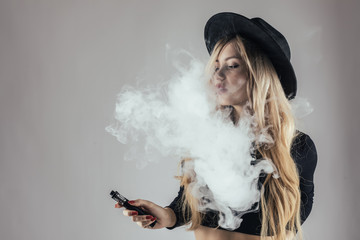 Young woman in black hat with e-cigarette make smoke cloud isolated on white background