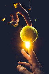 A male hand holding a tennis ball on an isolated dark background - 3D render - obrazy, fototapety, plakaty